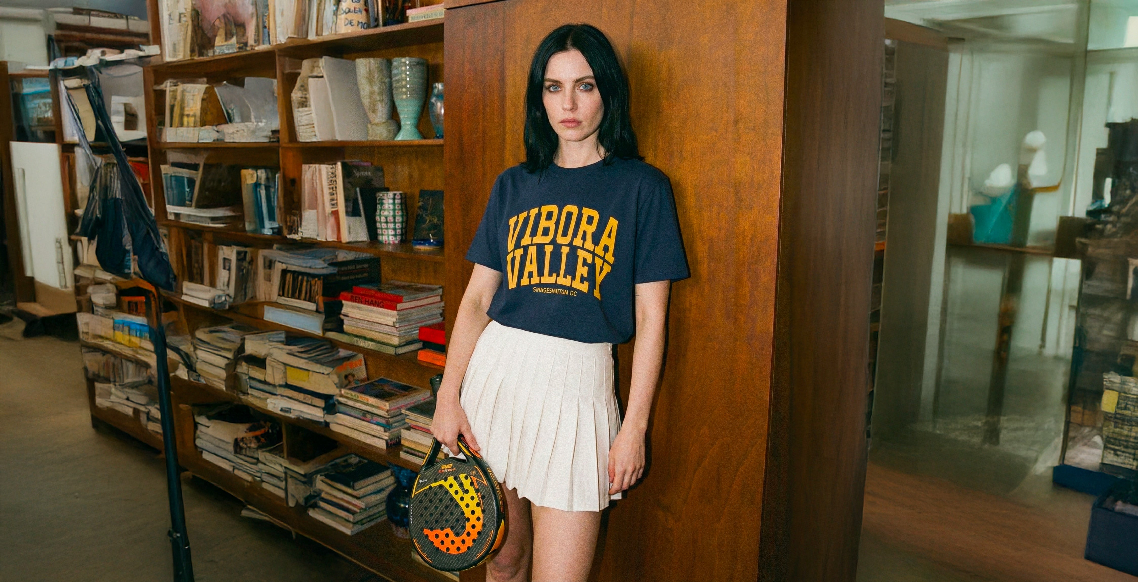 Woman in a bookstore wearing a 'Vibora Valley' padel t-shirt, holding a padel racket.