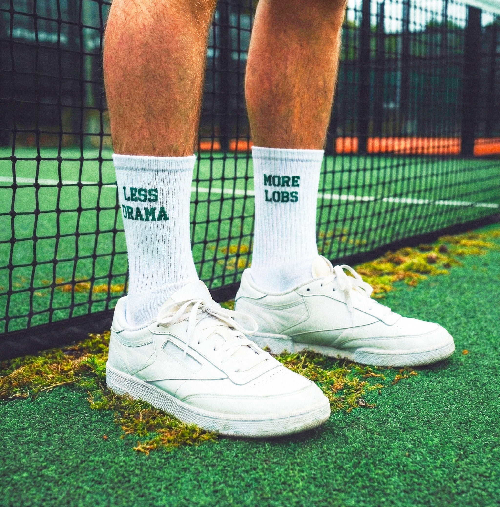 Person wearing white sneakers and socks with more lobs less drama on a padel court
