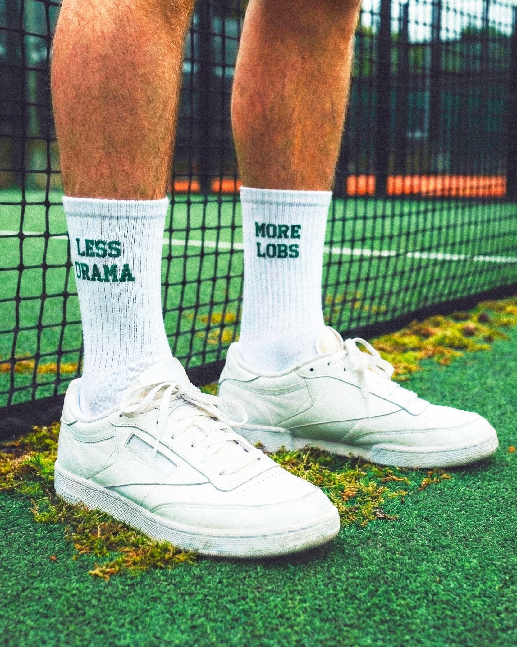 Person wearing white sneakers and socks with more lobs less drama on a padel court