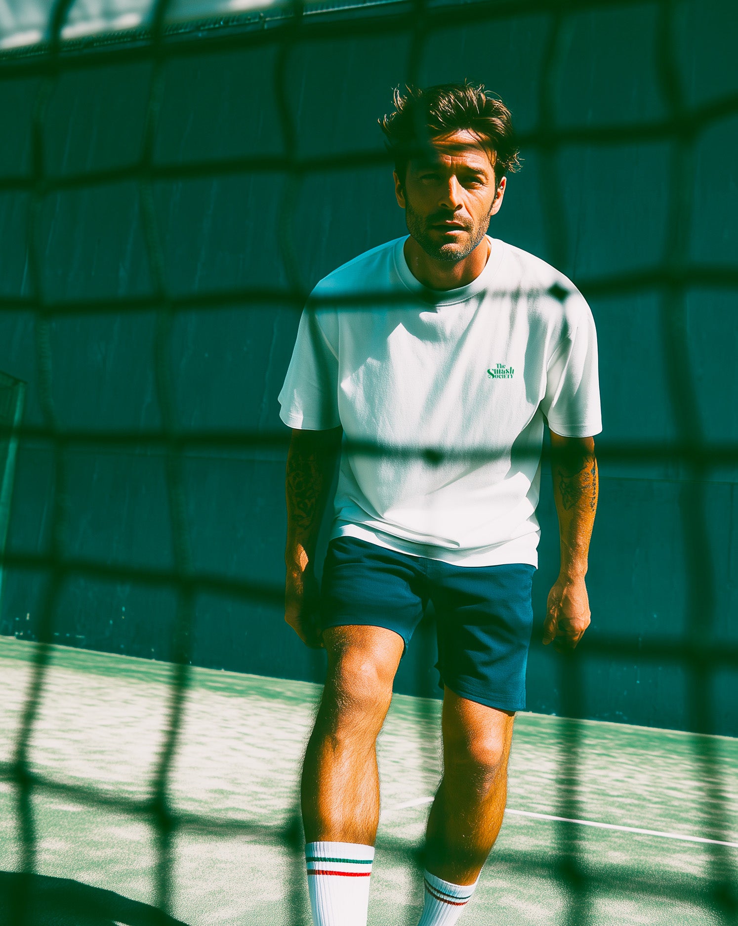 Man with a white padel t-shirt standing on a padel court with a net in the foreground