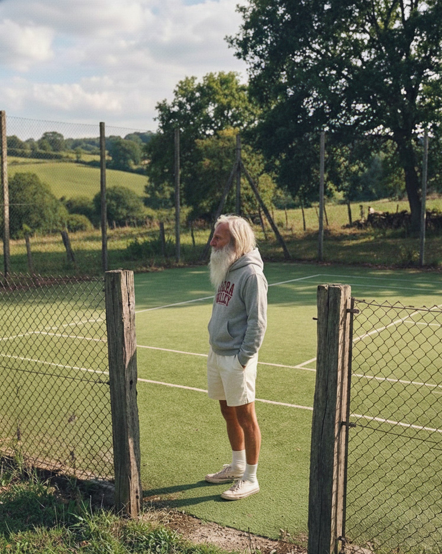 Person standing on a tennis court with a scenic background and wearing a grey vibora valley padel hoodie