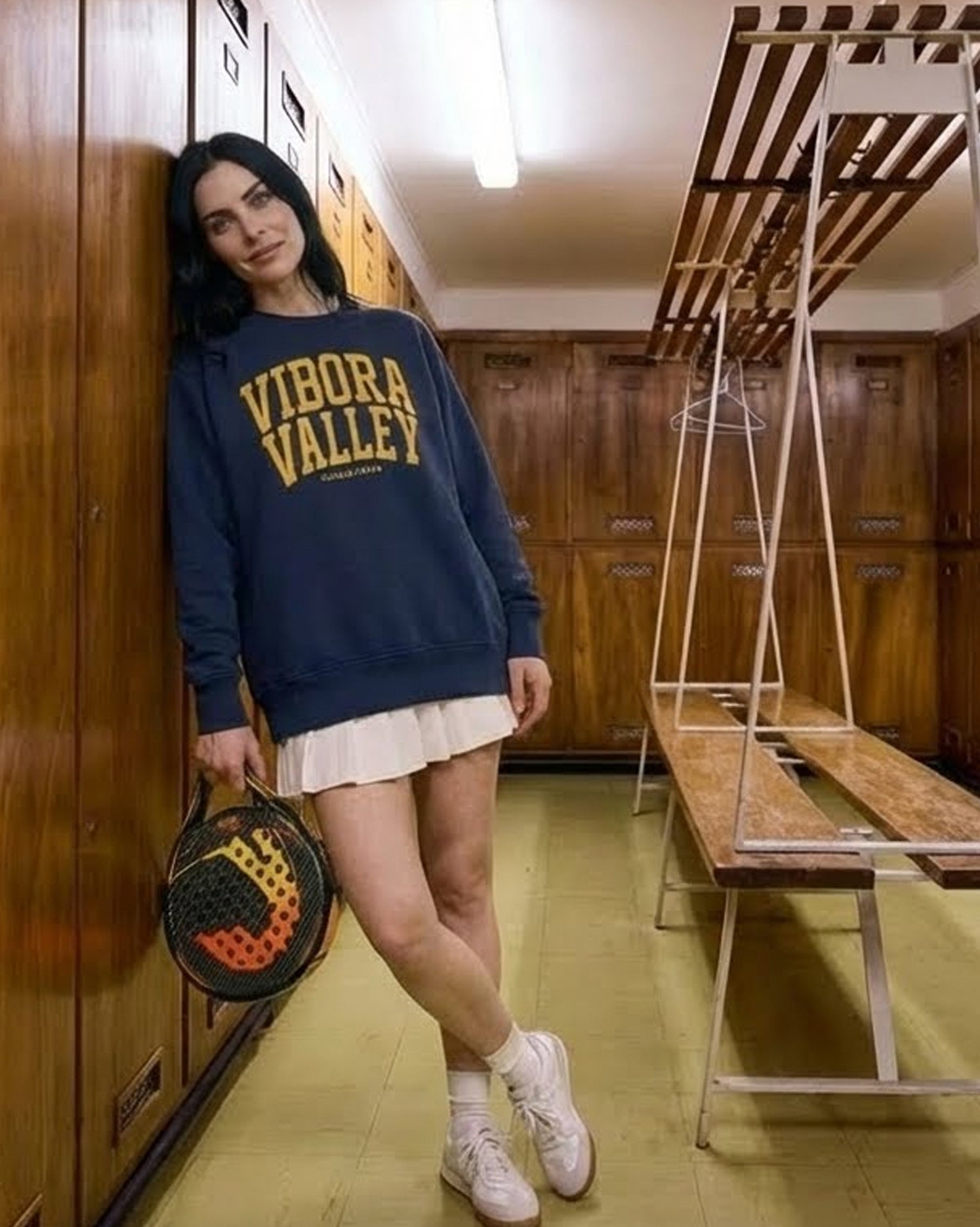 Person wearing a blue padel sweatshirt with 'Vibora Valley' text in a wooden locker room.