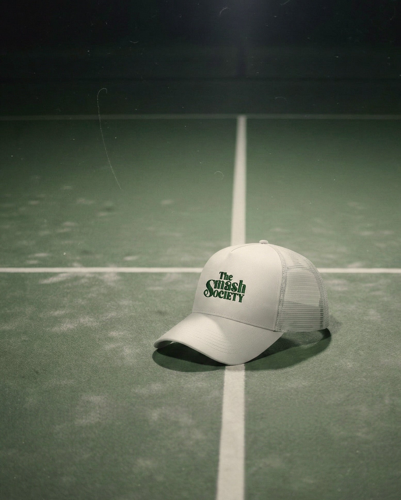 White cap with 'The Squash Society' logo on a padel court