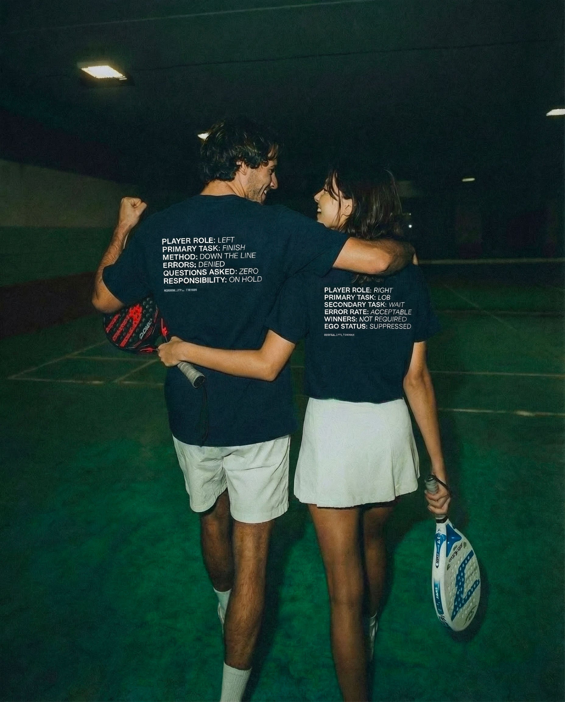 Two people on a padel court wearing matching dark blue shirts with text.